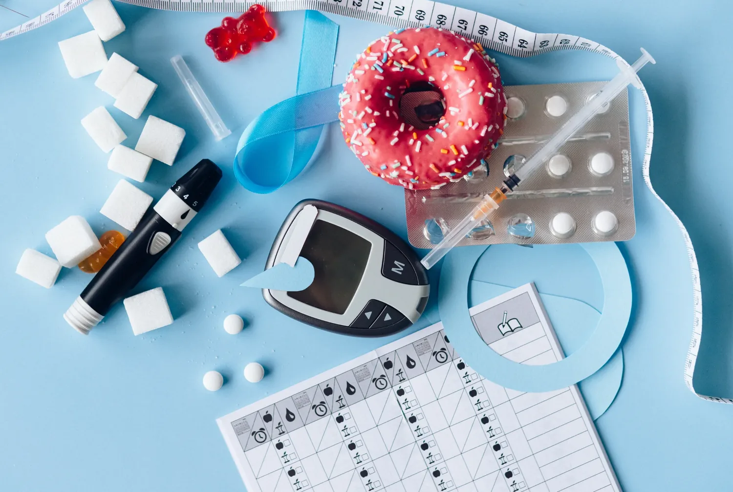 A flat lay showing a blood glucose meter, medication, a monitoring log sheet and a sweet pastry, illustrating the daily record keeping that diabetes care can involve